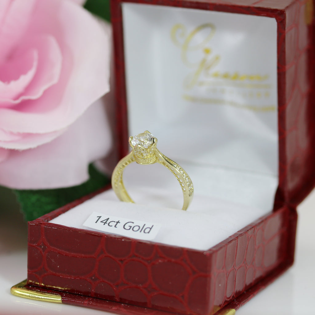 Side-angle view of 14ct gold Queen’s Crown CZ ring positioned inside a textured red ring box.