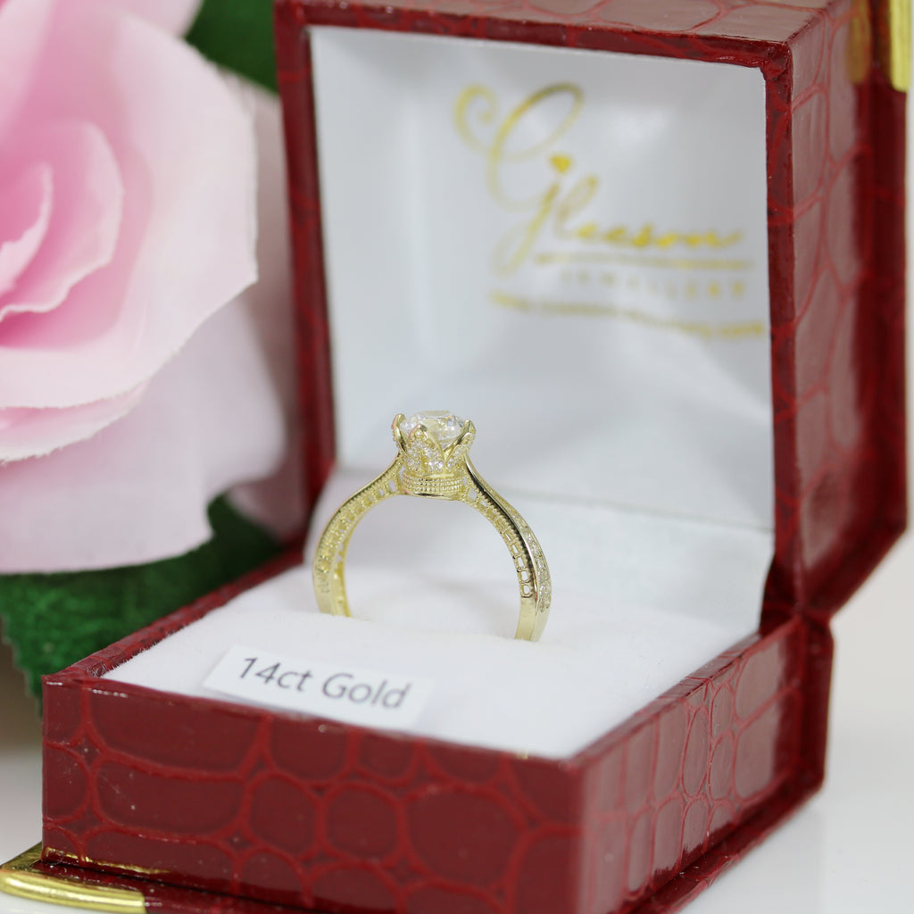 14ct yellow gold Queen’s Crown style CZ engagement ring displayed upright inside a red Gleeson Jewellers ring box with pink roses in the background.