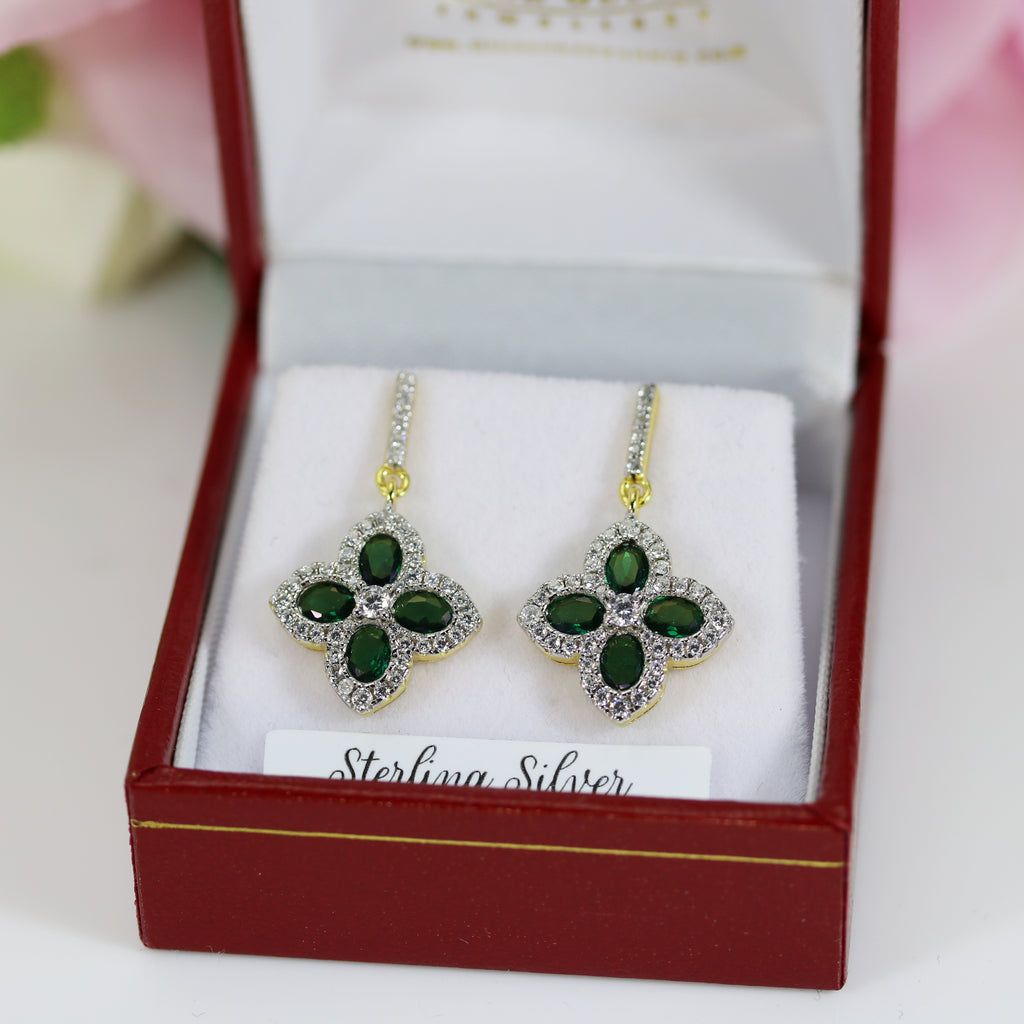 Side view of sterling silver emerald and cubic zirconia cluster drop earrings with a 14-carat gold vermeil finish, set in a Daniel Gleeson Jewelers jewelry box, highlighting the delicate drop design and sparkling gemstones