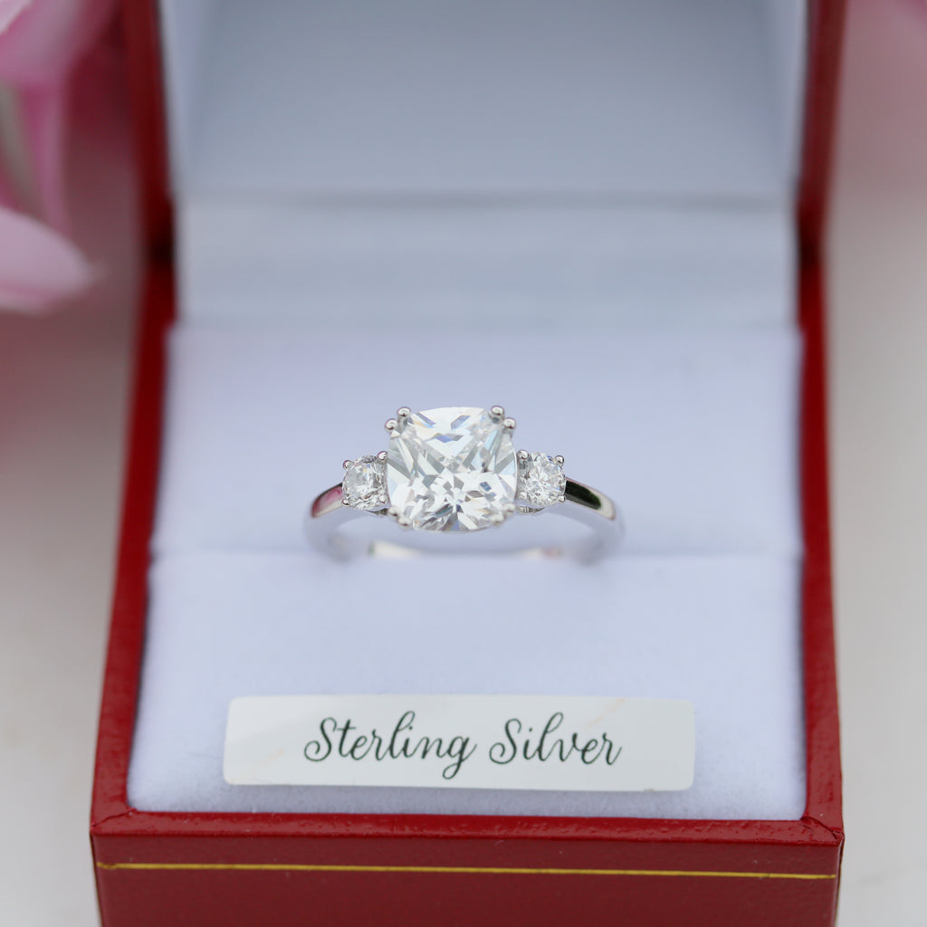 Close-up view of a sterling silver trilogy ring with a cushion-cut center cubic zirconia, displayed in a red Gleeson Jewellers ring box.