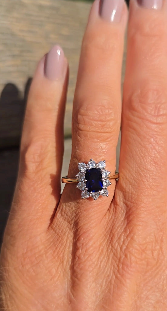 Close-up of the sapphire cluster ring on a hand, the vivid blue centre stone surrounded by bright cubic zirconia, from Gleeson Jewellers.