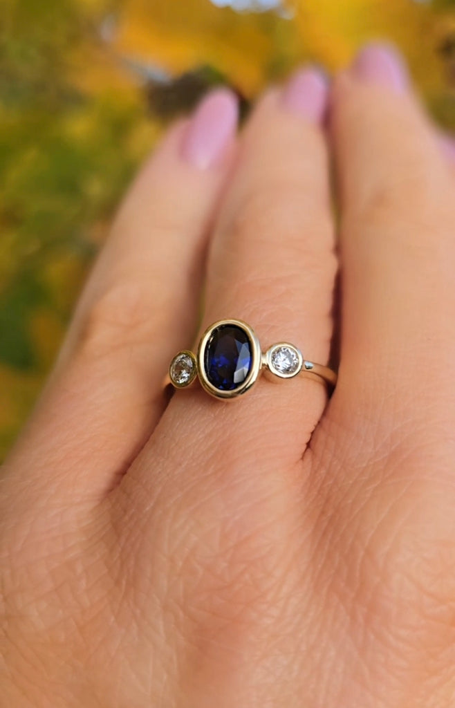 9ct Gold sapphire with a blue gemstone on a person's finger against a blurred natural background