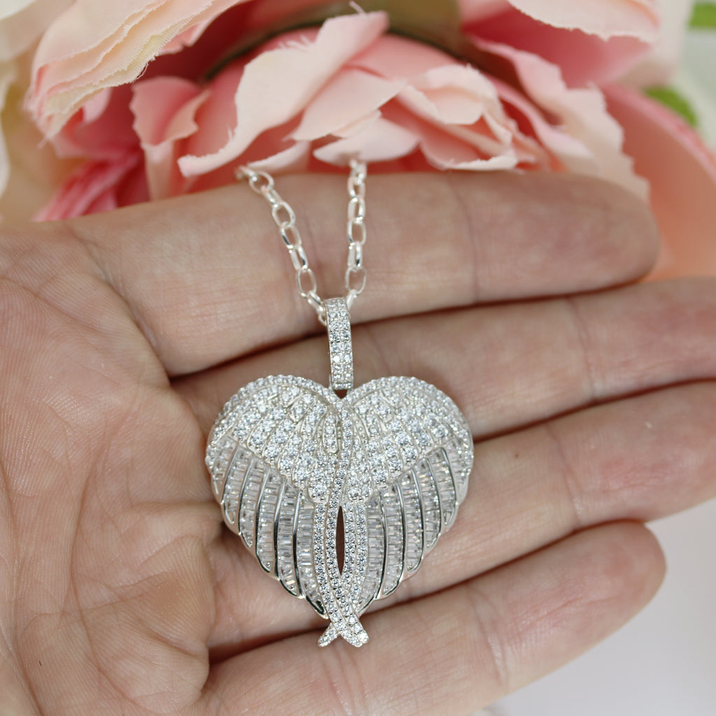 Close-up of a sterling silver heart-shaped angel wings pendant encrusted with cubic zirconia stones, held in hand to showcase size and intricate details