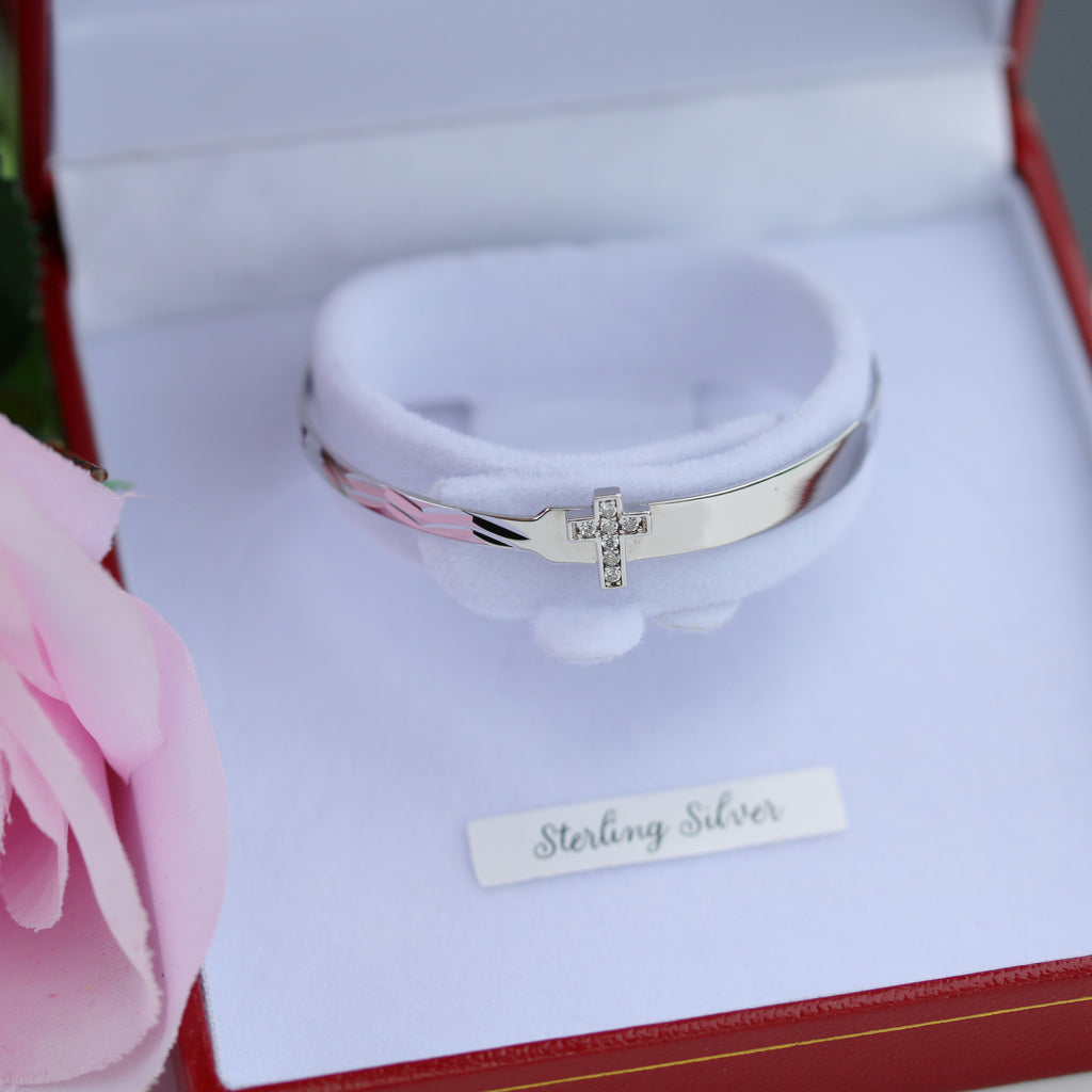 Overhead view of sterling silver baby ID bangle with cross detail, presented in Gleeson Jewellers packaging.