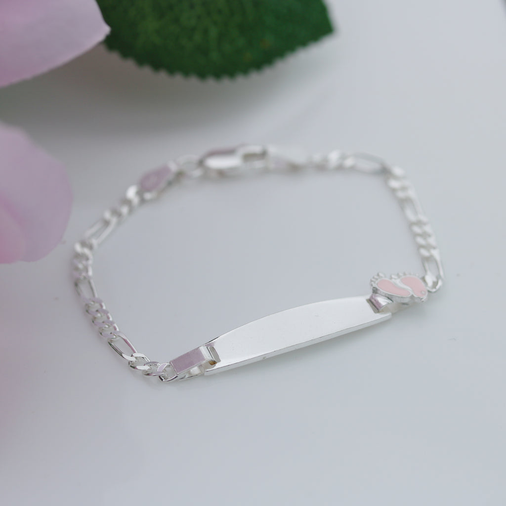 Sterling silver Figaro chain kids bracelet with engraved plate and pink baby feet accent, photographed on a white background.