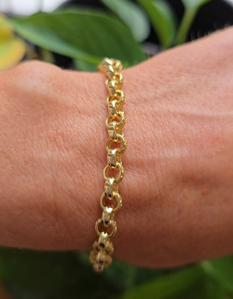 Gold on sterling silver patterned belcher-link bracelet shown worn on a wrist, photographed outdoors with greenery in the background