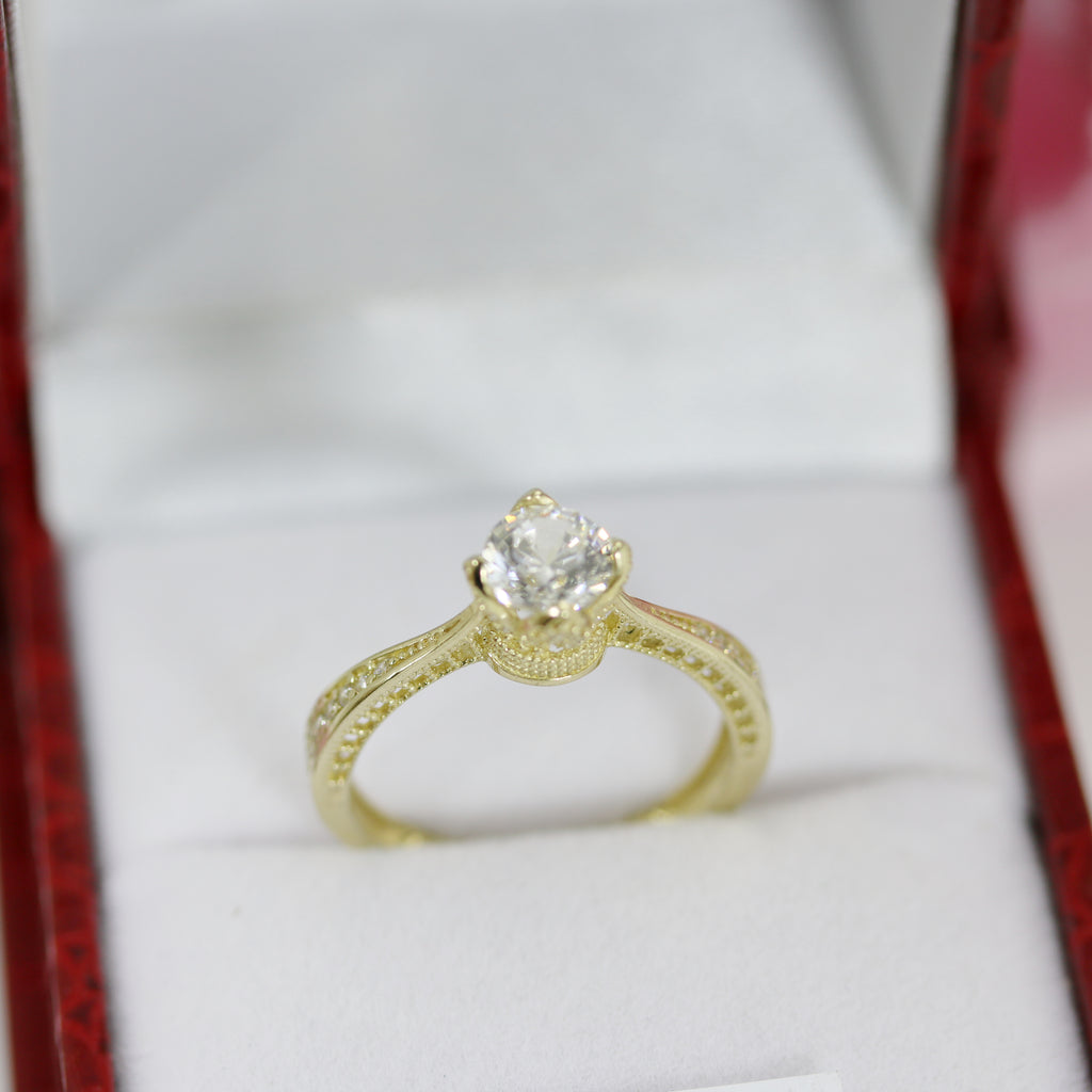 Front-facing view of 14ct yellow gold CZ crown ring on display inside a red jewellery box, pink roses softly blurred in the background.