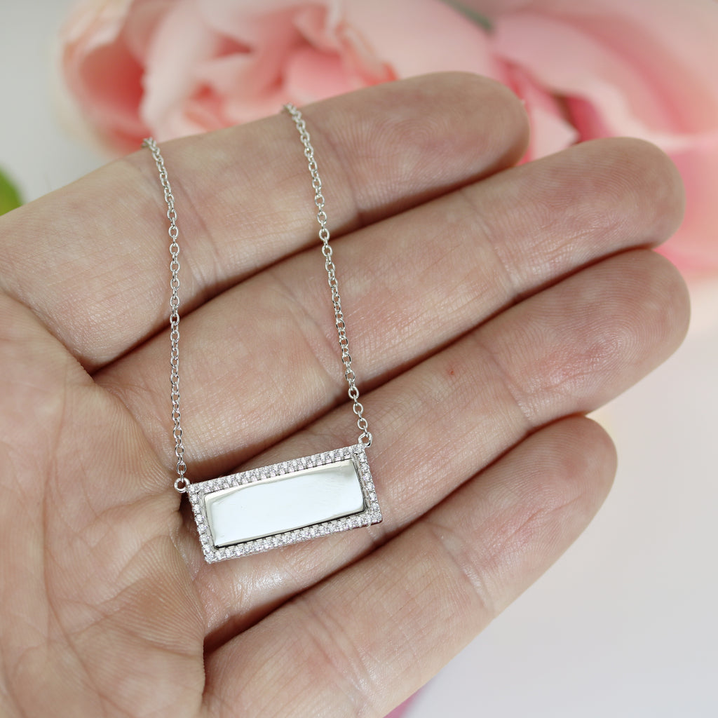 Close-up of a sterling silver engravable pendant necklace with a CZ border, held in hand to show size and delicate chain detail