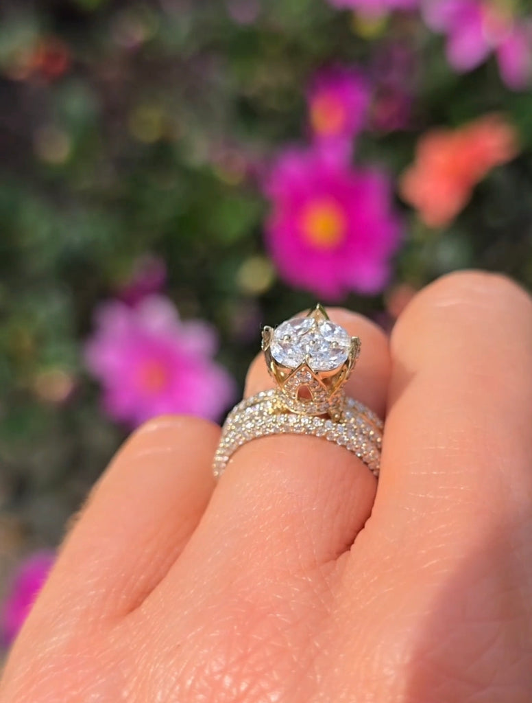 Hand wearing the Clíona 14ct gold bridal ring set by Gleeson Jewellers, shown against pink garden flowers.