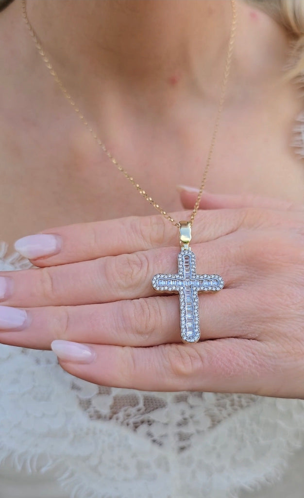 Close-up of 9ct gold baguette and round CZ cross pendant resting on fingers, highlighting polished gold and stone clarity.

