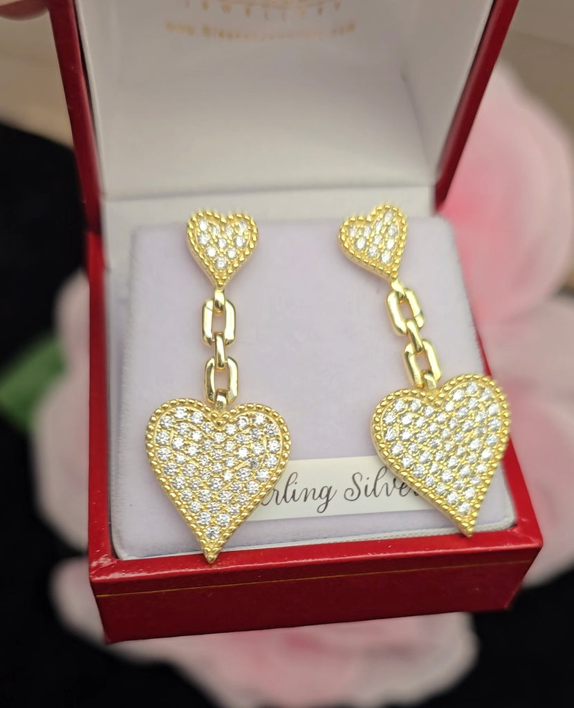 Gold-plated heart drop earrings with cubic zirconia stones, displayed in a red jewellery box from Daniel Gleeson Jewellers, Cork. The earrings are angled to the left, showcasing their sparkling detail and chain-link design