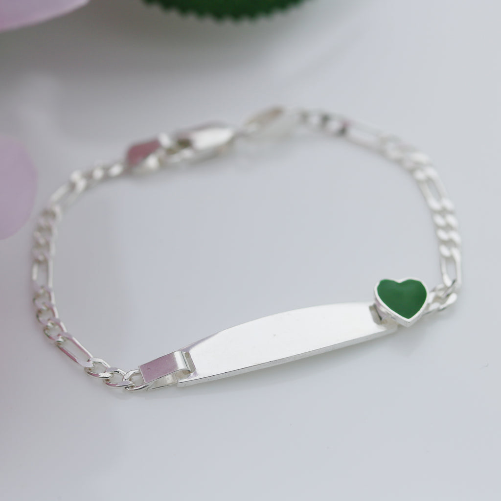 Sterling silver 6.5-inch children’s Figaro ID bracelet with smooth plate and green enamel heart, displayed on a white background with pink flower and green leaf detail from Gleeson Jewellers