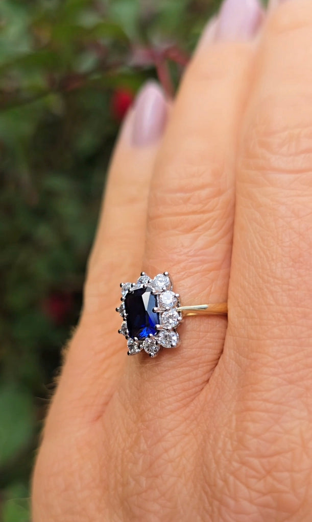 Side view of the sapphire cluster ring on a hand, showing the gold band and halo of stones from Gleeson Jewellers.