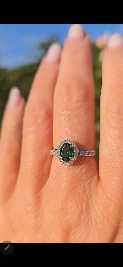 9ct gold emerald and cubic zirconia halo ring worn on a woman’s hand in natural light.
