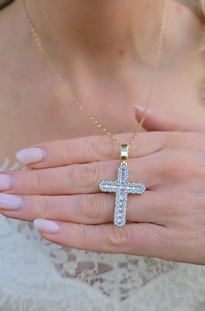 Detailed view of 9ct gold cross pendant with baguette-cut center stones and round CZ border, held in hand.