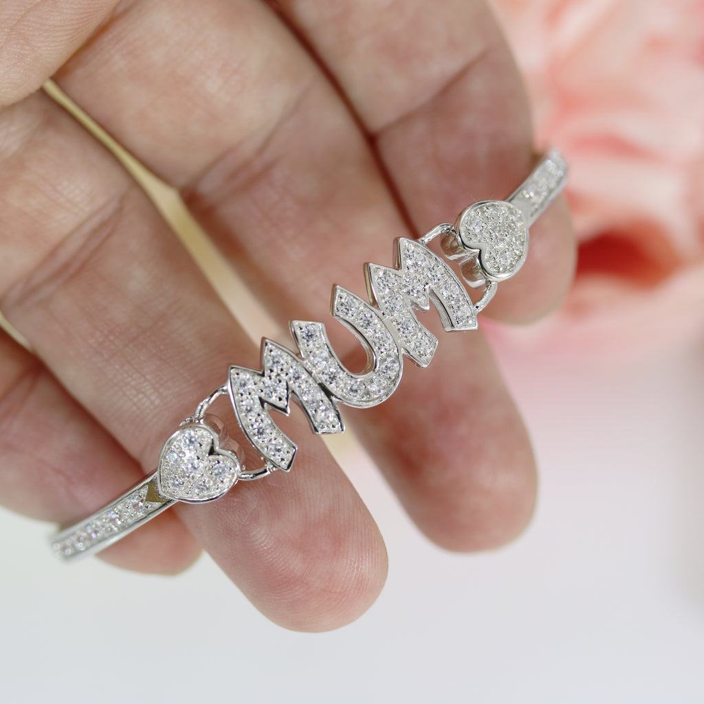 Close-up of a sterling silver Mum bangle bracelet held in hand, showcasing its sparkling CZ design and heart details.