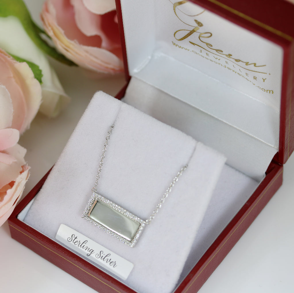 Sterling silver rectangular engravable pendant with a cubic zirconia border, elegantly displayed in a red and white jewelry box