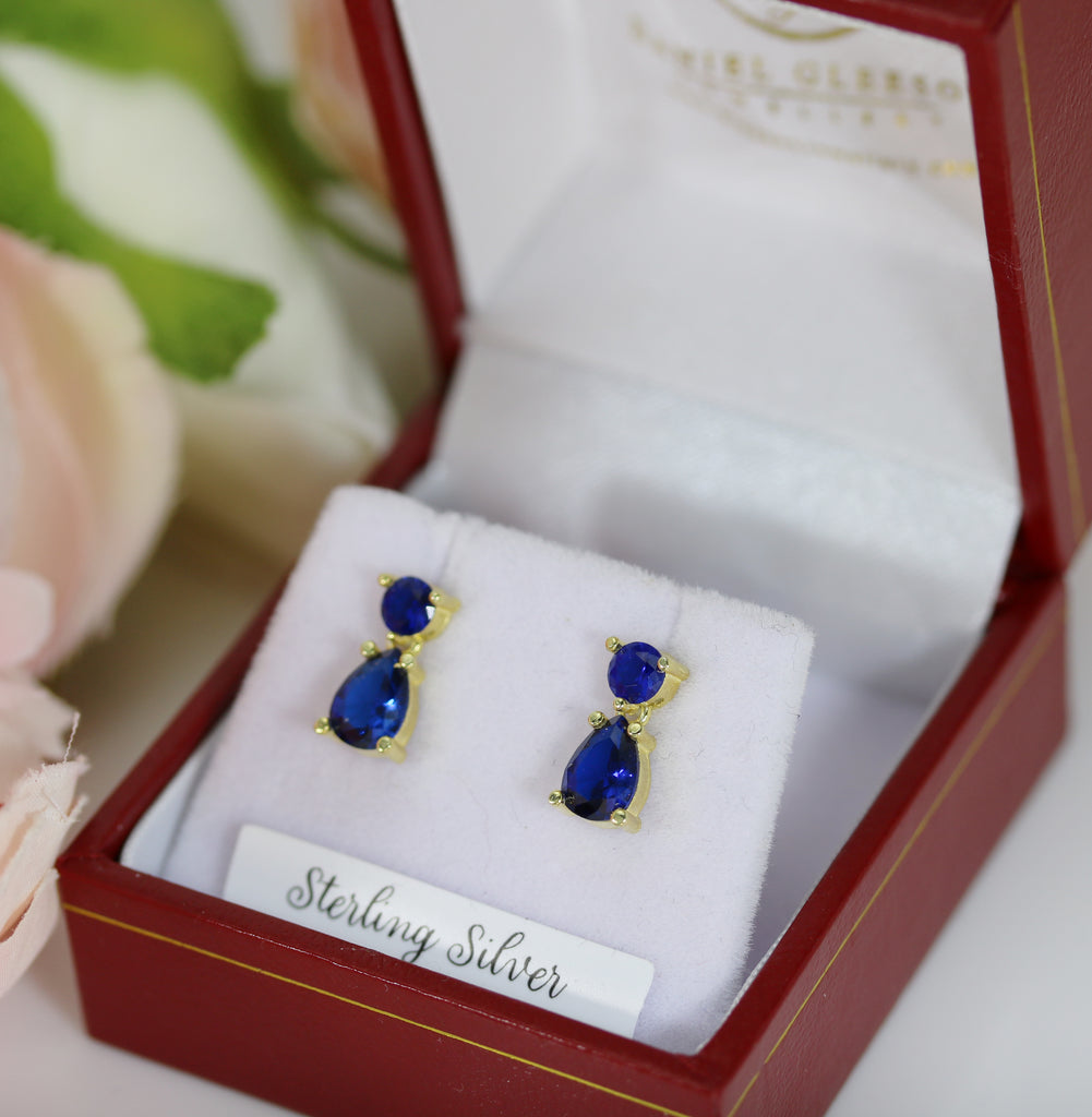 Close-up of sapphire blue cubic zirconia drop earrings with a 14ct gold finish, set in sterling silver, beautifully presented in a luxury gift box