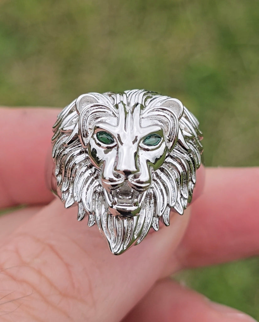 Close-up front view of sterling silver lion head ring with green CZ eyes, held between fingers from gleeson jewellers 