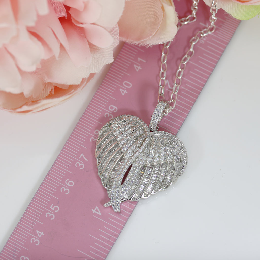 Large sterling silver angel wings heart pendant with sparkling cubic zirconia, placed next to a pink ruler for size comparison