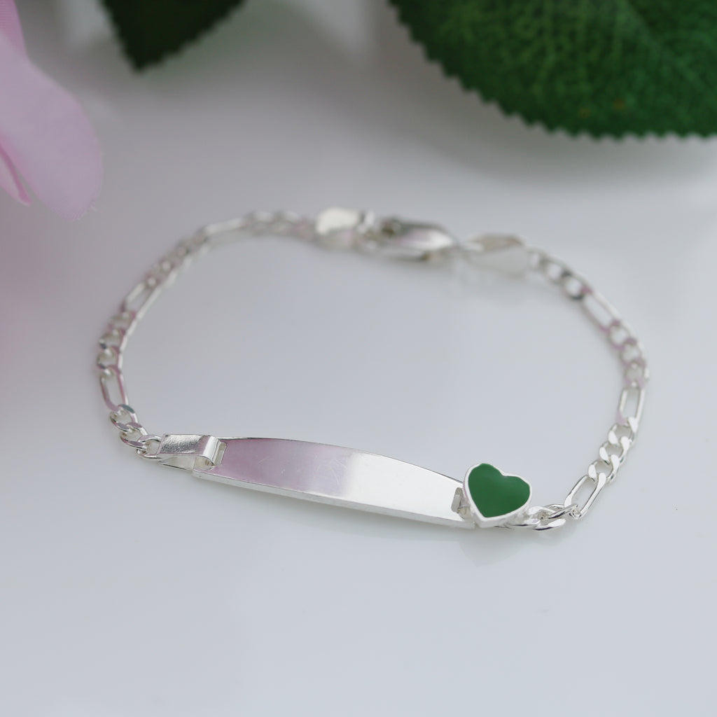 Sterling silver Figaro chain kids bracelet with engraved plate and green heart accent, photographed on a white background.