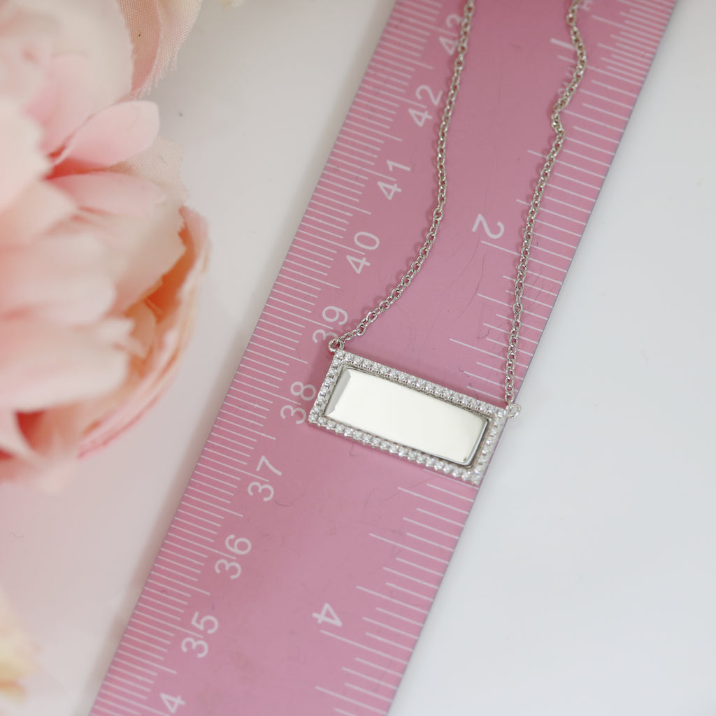 Sterling silver rectangular pendant with cubic zirconia border placed next to a pink ruler, showing its compact and elegant size