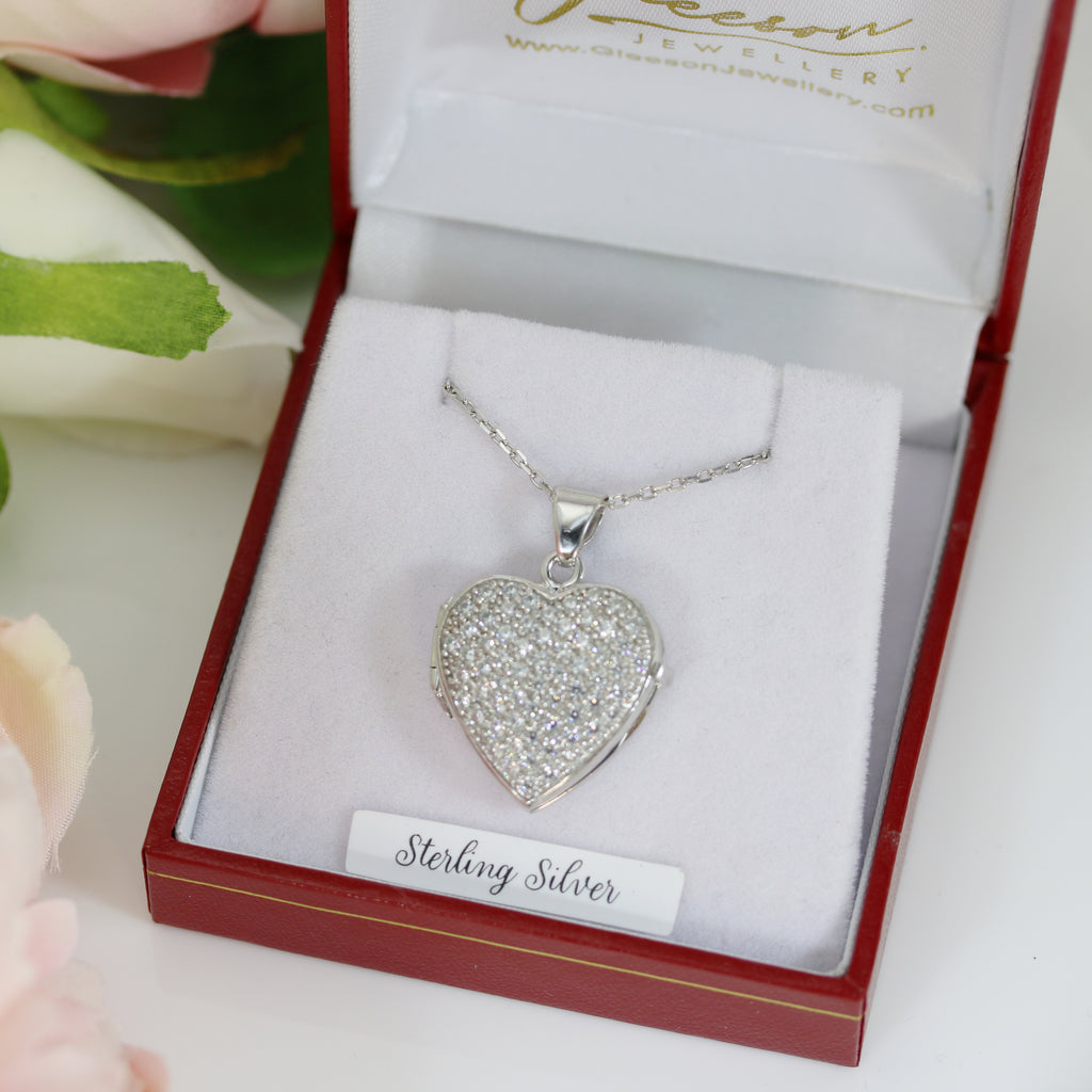 Sterling silver heart-shaped locket encrusted with cubic zirconia stones, displayed in a luxurious red and white jewelry box