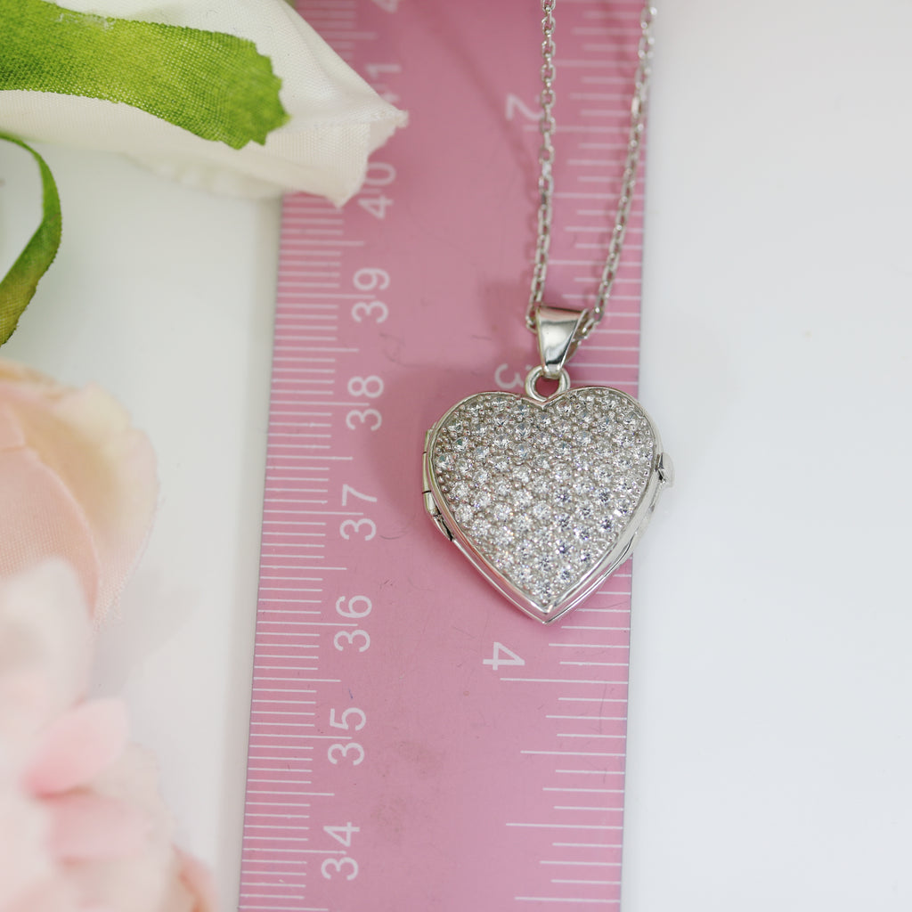 Sterling silver CZ heart locket placed beside a pink ruler, showing its compact and elegant size