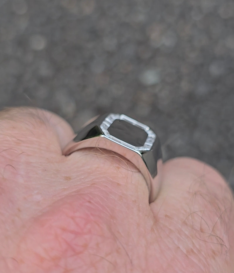 Side angle of a sterling silver men's signet ring with a polished surface and baguette CZ border, worn on hand.
