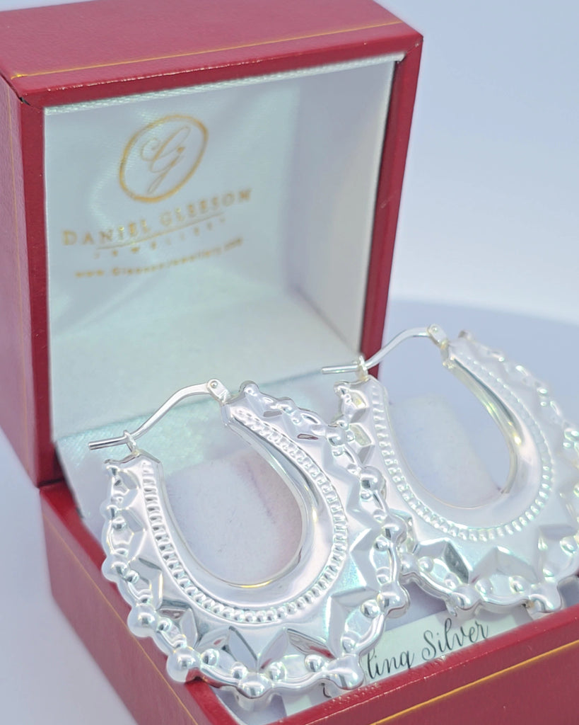Elegant spike creole earrings by Gleeson Jewellers angled in a red box under sunlight.