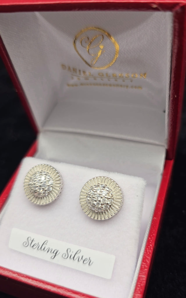 Elegant and eye-catching, these sterling silver disc stud earrings are inspired by the timeless style of Rolex. Featuring a center pavé of cubic zirconia, they add a touch of sparkle to any outfit. Crafted by Daniel Gleeson Jewellers in Cork, they come beautifully presented in a red gift box, perfect for gifting or personal luxury