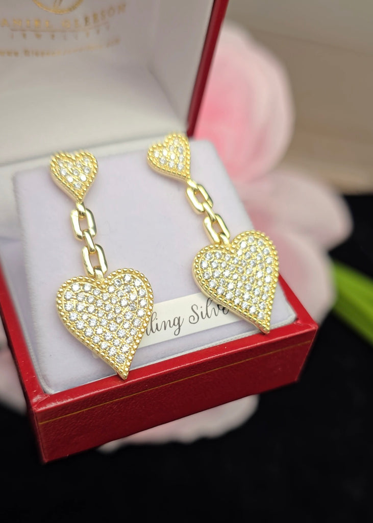 14K gold-plated sterling silver heart drop earrings adorned with cubic zirconia stones, presented in a red jewellery box from Daniel Gleeson Jewellers, Cork. The earrings are positioned to the right, emphasizing the intricate chain-link and pave details