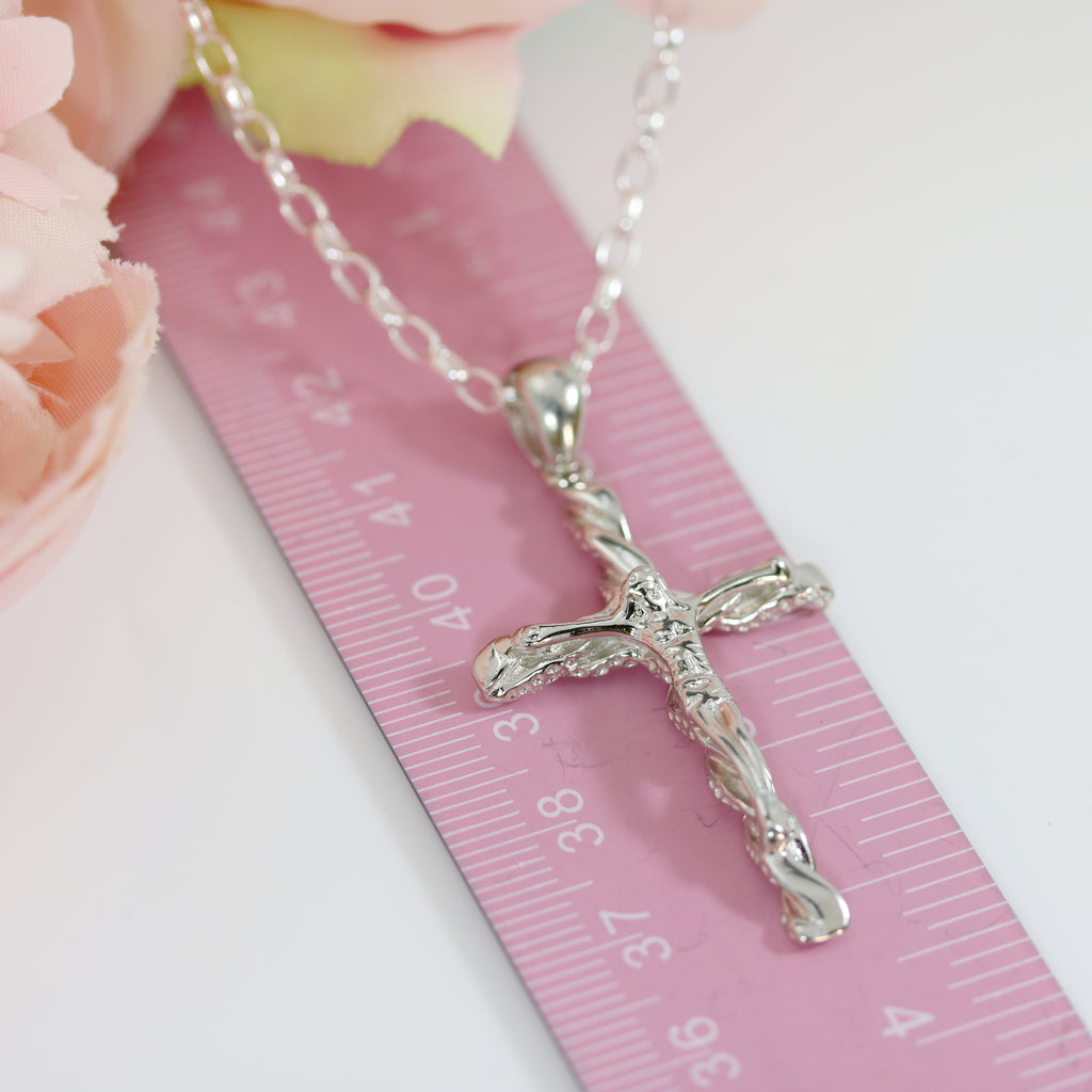 Sterling silver textured cross pendant with Jesus figure displayed on a pink ruler, showing its length and intricate craftsmanship