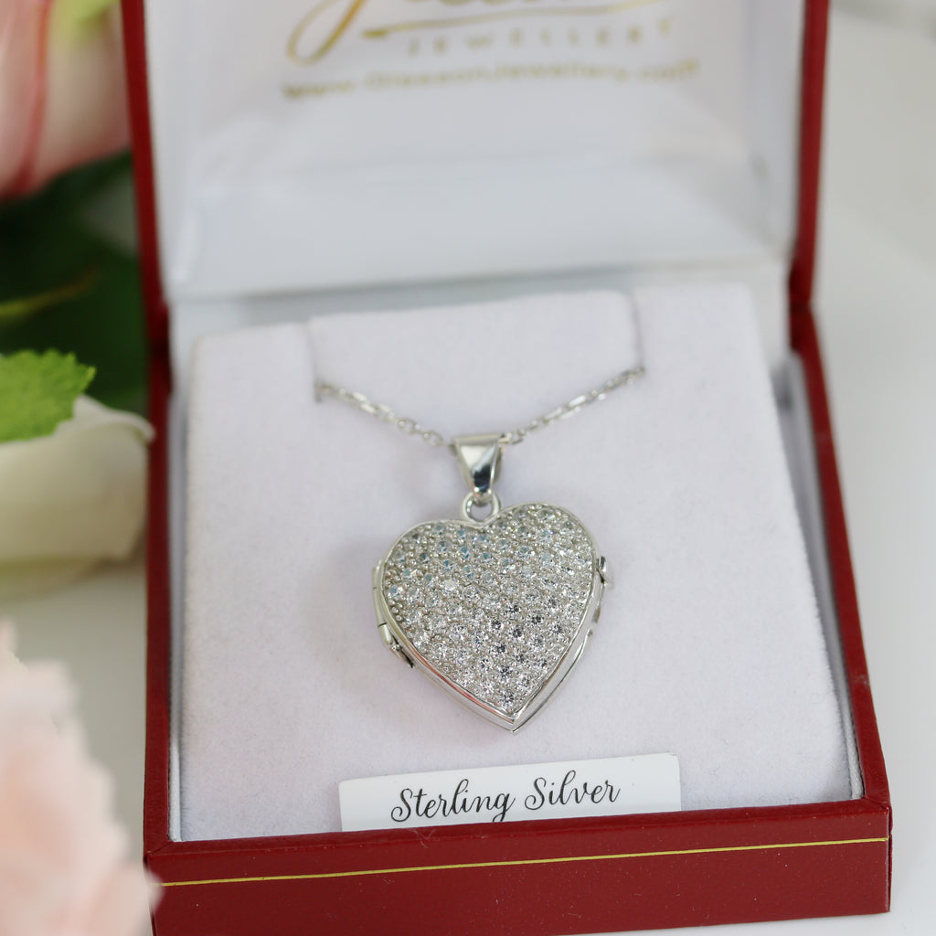 Diamond-encrusted sterling silver heart locket in a red jewellery box with a delicate silver chain, surrounded by soft floral accents