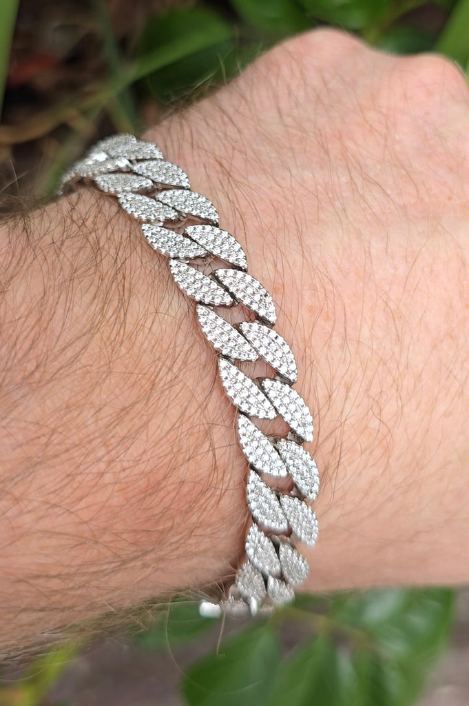 Close-up of a men's sterling silver CZ-encrusted Cuban bracelet worn on wrist, photographed outdoors with greenery in the background.