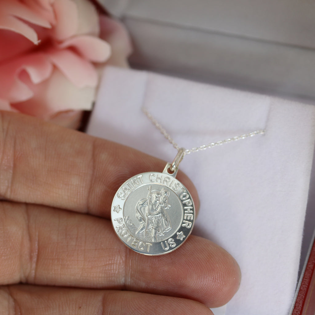 Close-up of a sterling silver Saint Christopher pendant being held in hand, showcasing the detailed engraving and polished finish