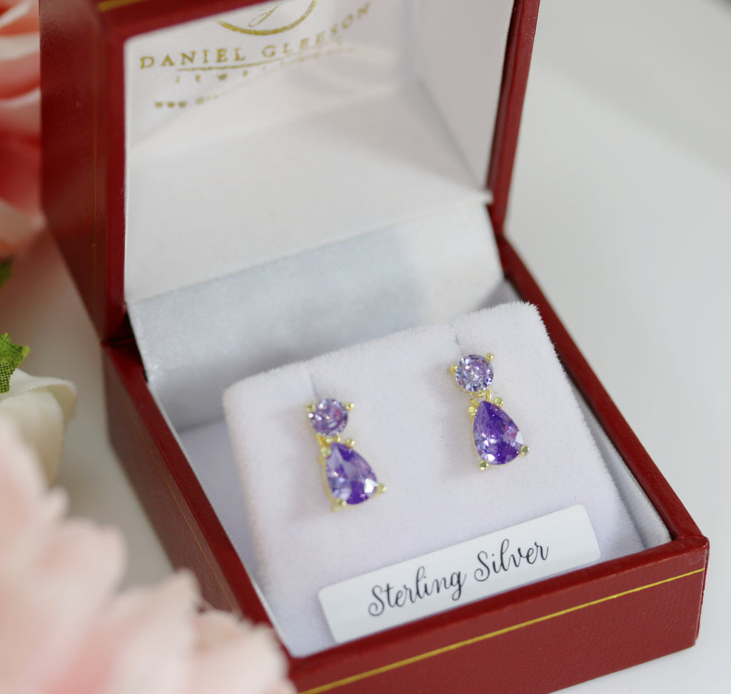 A pair of sterling silver drop earrings with amethyst-coloured cubic zirconia stones, elegantly presented in a luxurious red jewellery box