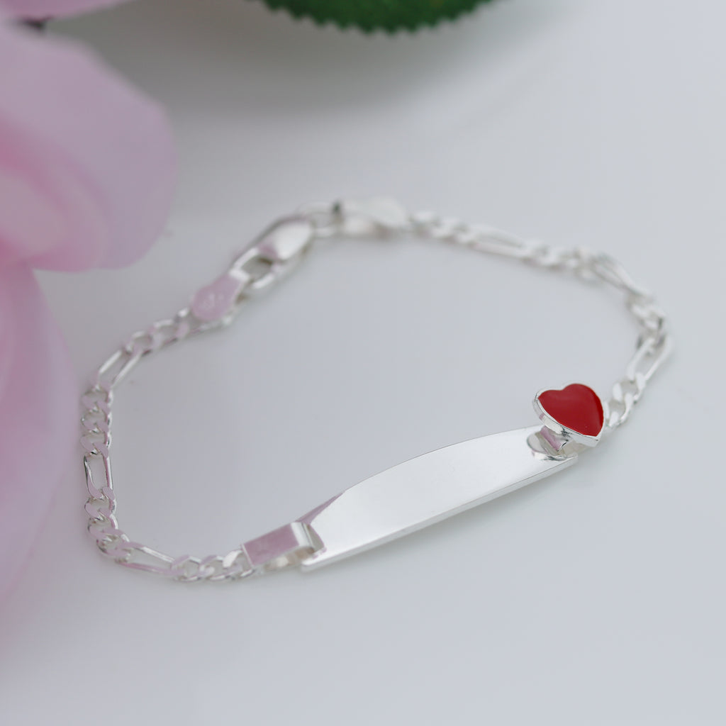 Sterling silver 6.5-inch children’s Figaro ID bracelet with smooth plate and red enamel heart, displayed on a white background with pink flower and green leaf detail from gleeson jewellers 