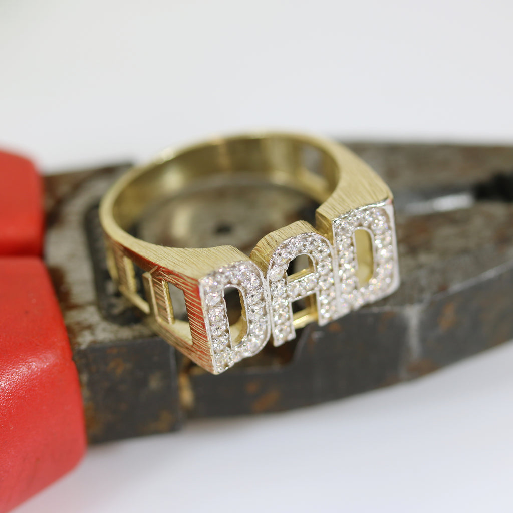 Angled view of the DAD Ring on a jeweller's tool – A side perspective of the ring, showcasing the solid gold band, open linked sides, and the cubic zirconia detailing on the initials.