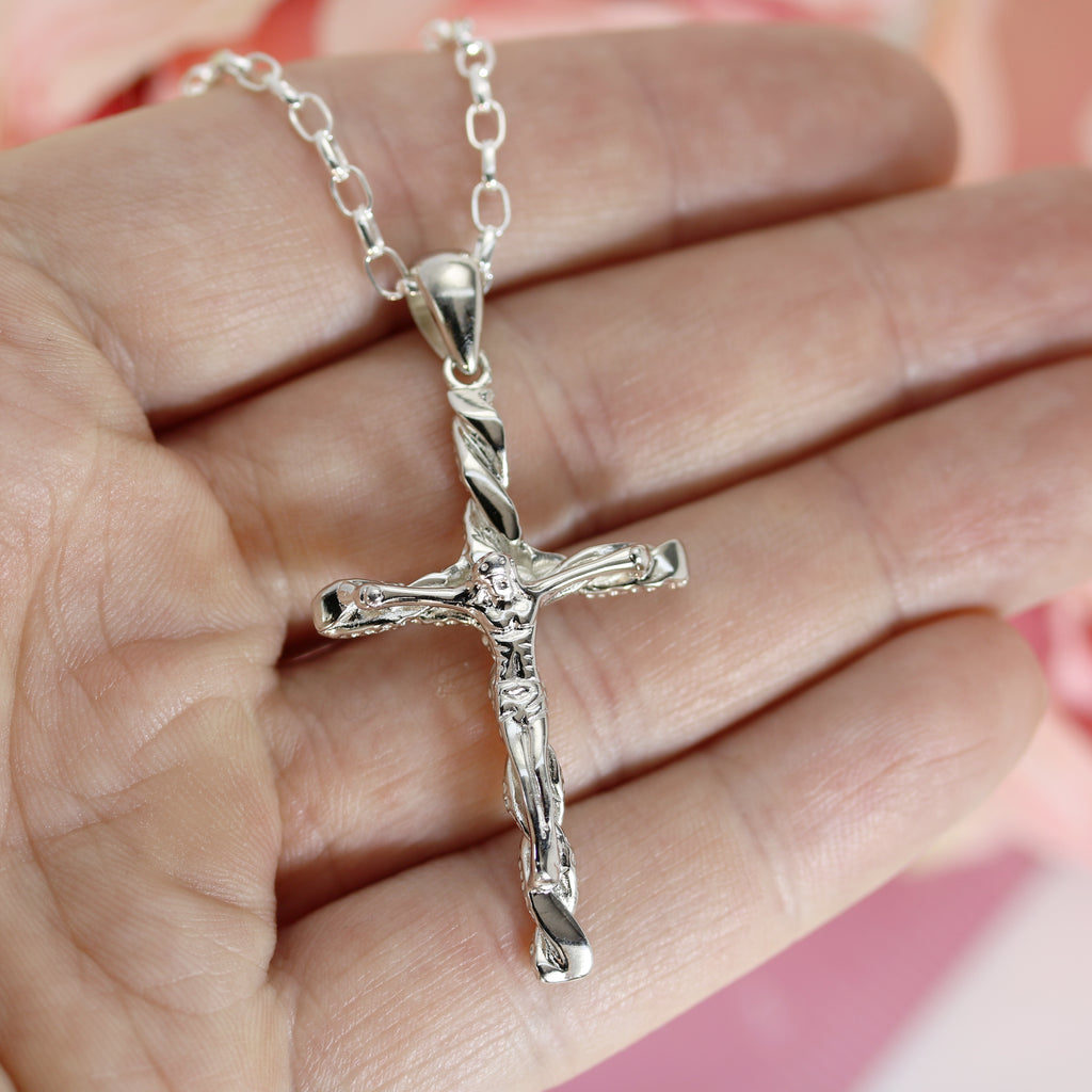 Close-up of a sterling silver crucifix necklace held in hand, highlighting the textured cross design and Jesus figure in fine detail.