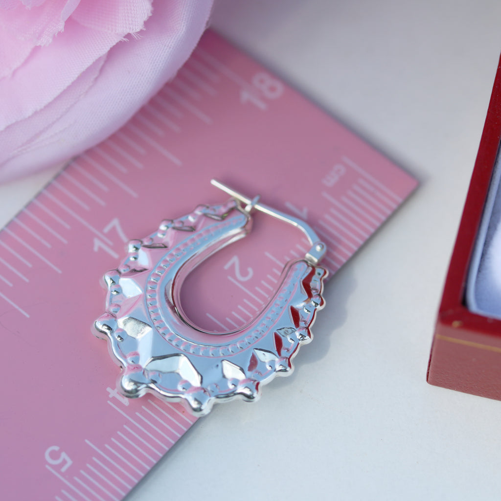 Close-up of a single oval spiked creole earring from Gleeson Jewellers next to a pink ruler for size reference.