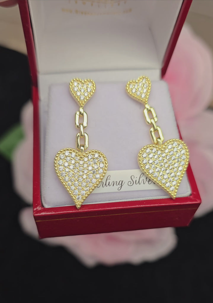 A close-up video of gold-plated heart drop earrings with cubic zirconia stones, elegantly displayed in a red jewelry box from Daniel Gleeson Jewellers, Cork. The video highlights the sparkling detail, chain-link design, and luxurious craftsmanship of the earrings