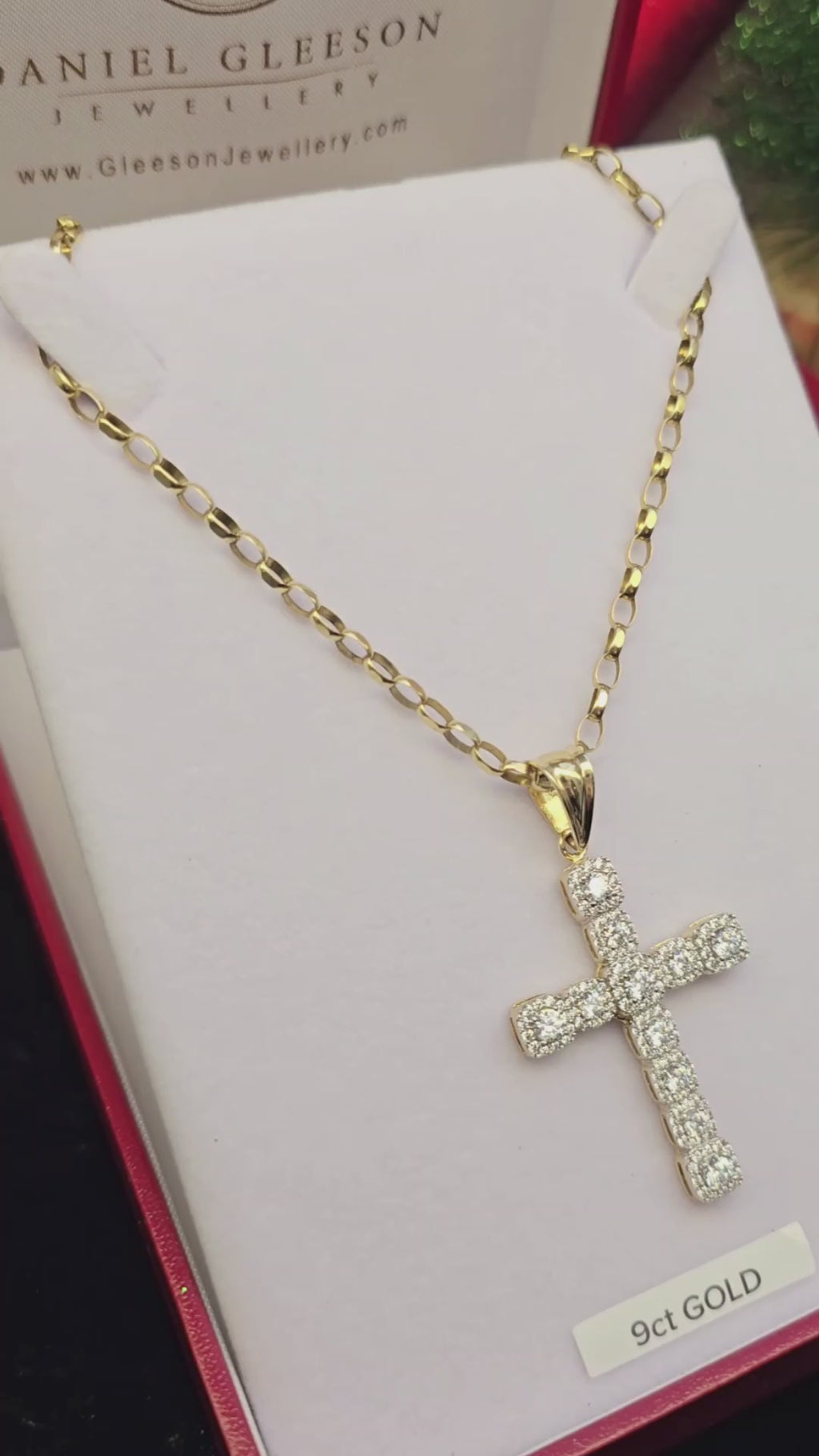 Video close-up of sturdy gold cross pendant with halo-set stones on belcher chain in a gleeson jewellers gift box and also demonstrated on the hand for size context.