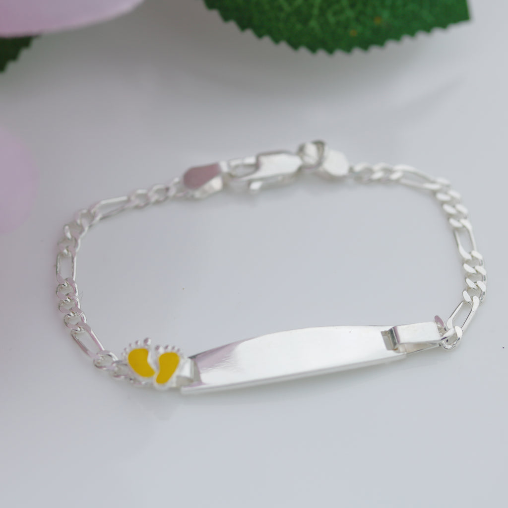 Sterling silver Figaro chain kids bracelet with engraved plate and yellow baby feet accent, photographed on a white background