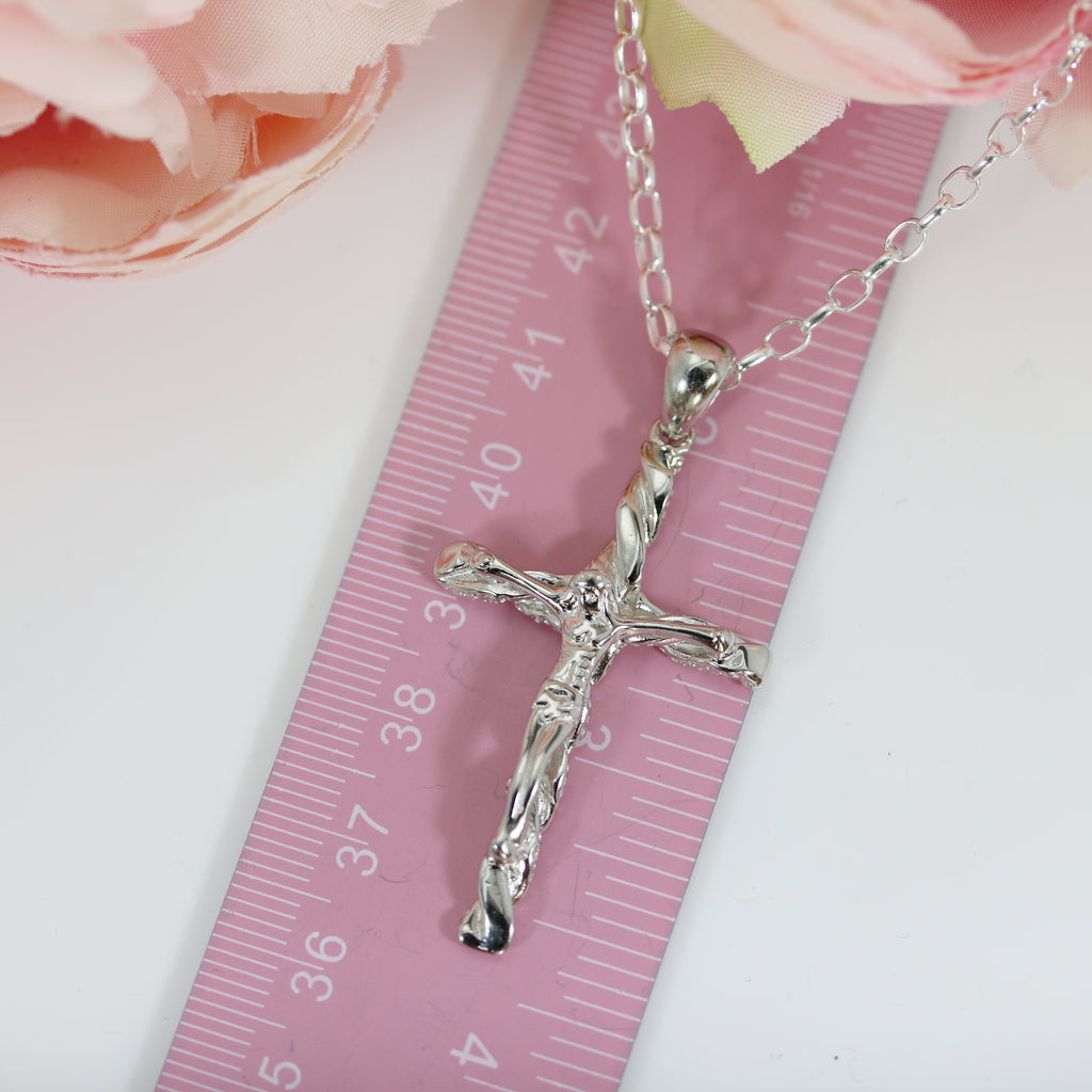 Solid sterling silver crucifix pendant placed next to a gleeson jewellers pink ruler for size reference, showcasing its detailed textured finish