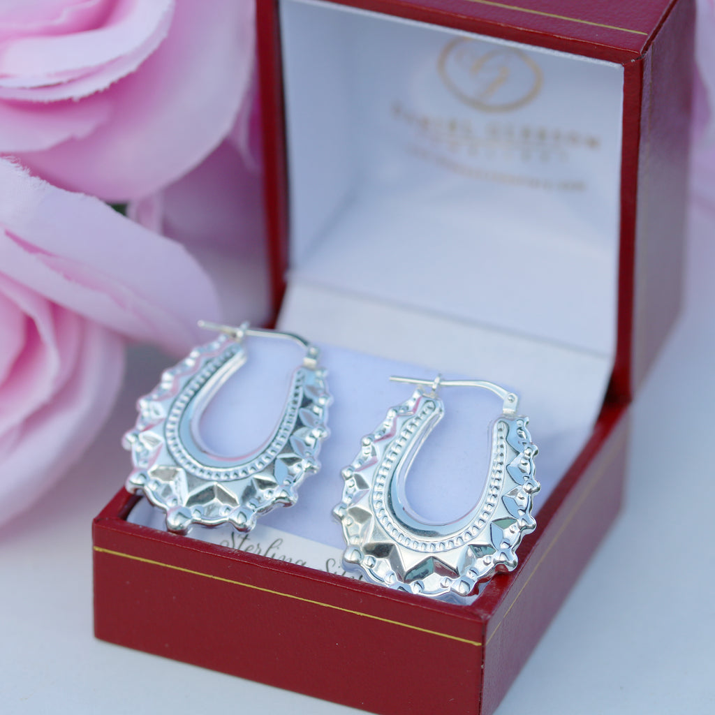 Pair of 925 sterling silver oval spiked creole earrings from Gleeson Jewellers shown in branded box with soft pink decor.