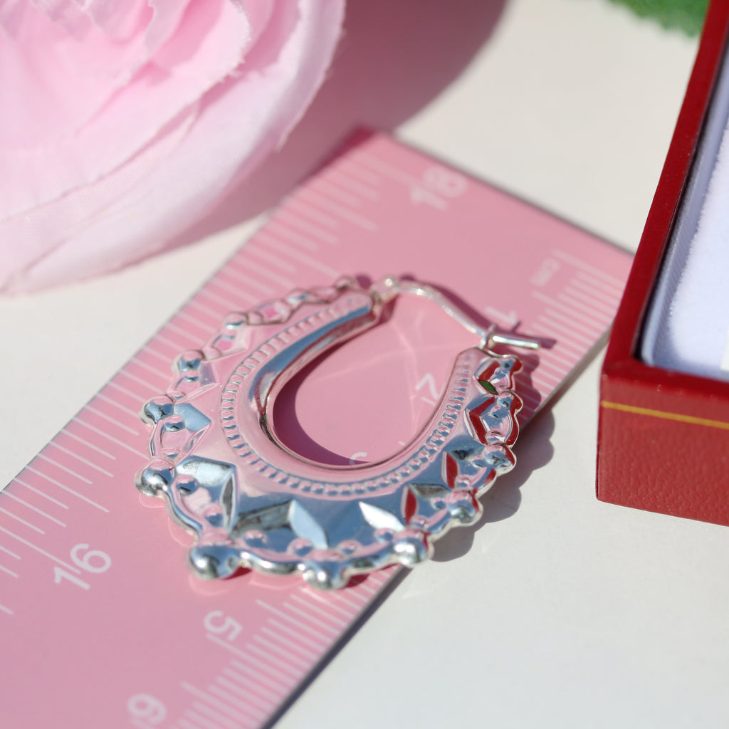 Close-up of a sterling silver creole earring by Gleeson Jewellers next to a pink ruler for size reference.