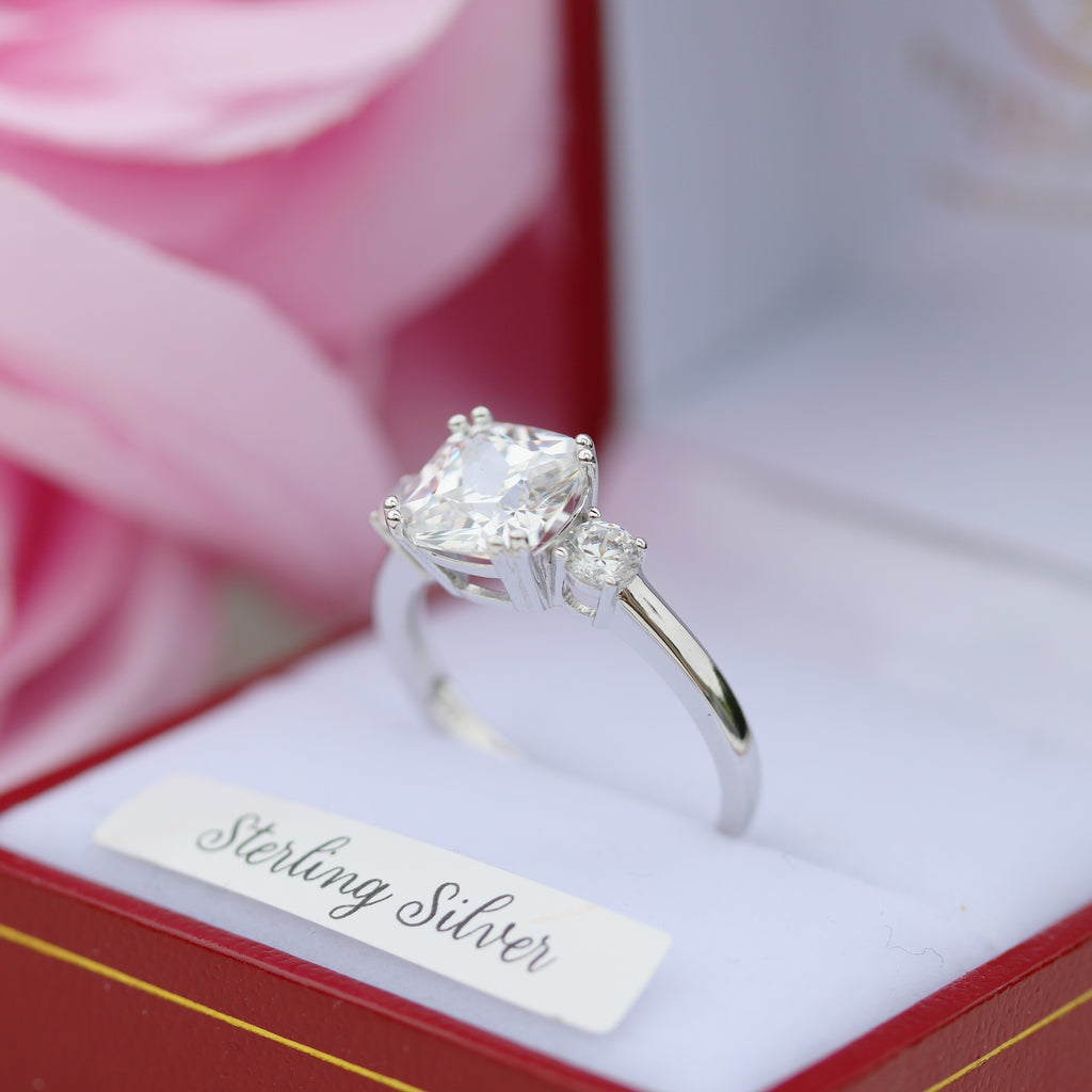 Side angle of the sterling silver trilogy ring with cubic zirconia stones, photographed in its box against a soft pink rose background.