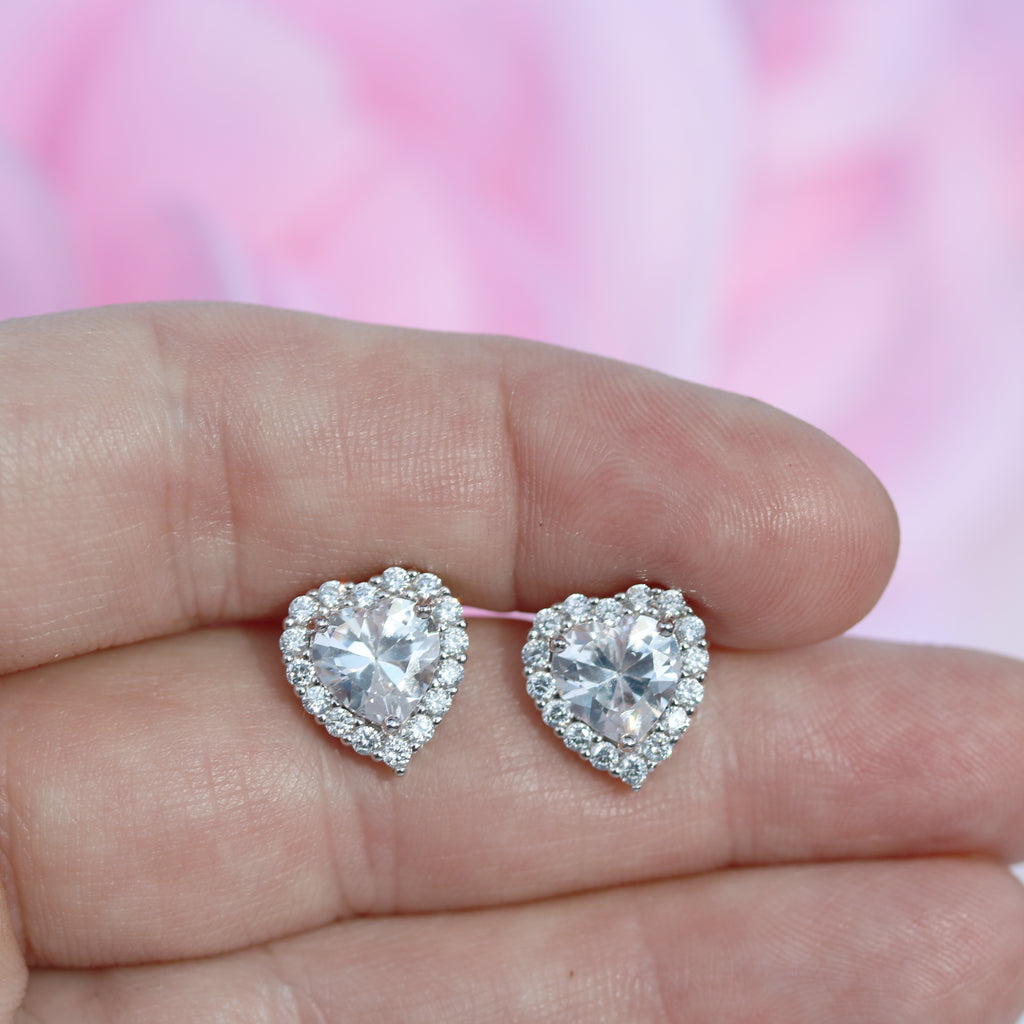 A pair of Sterling Silver Heart-Shaped CZ Halo Stud Earrings from Gleeson Jewellery, held in hand to showcase size and sparkle. Available online